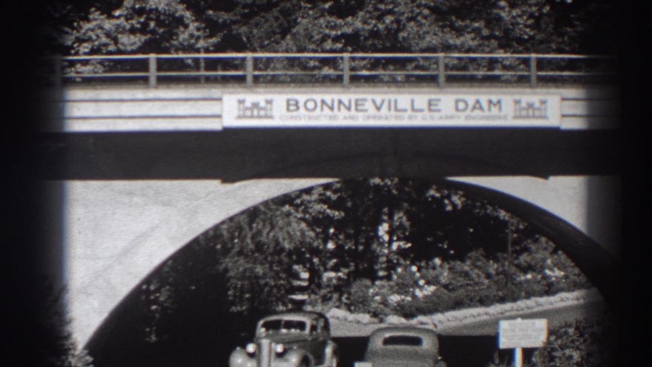 Cars pass under a concrete arch with a Bonneville Dam sign above.