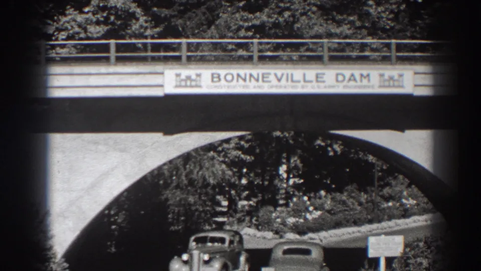 1938 8mm view at Bonneville Dam in Oregon, showing vintage cars beneath a concrete arch and a sign above the roadway.