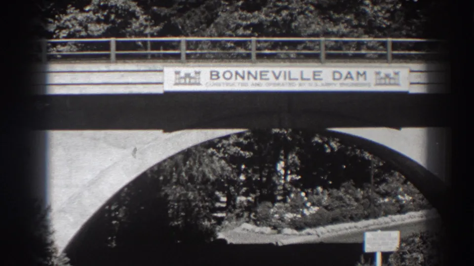1938 8mm view of the Bonneville Dam bridge sign with U.S. Army Engineers wording above a concrete arch and shaded trees.