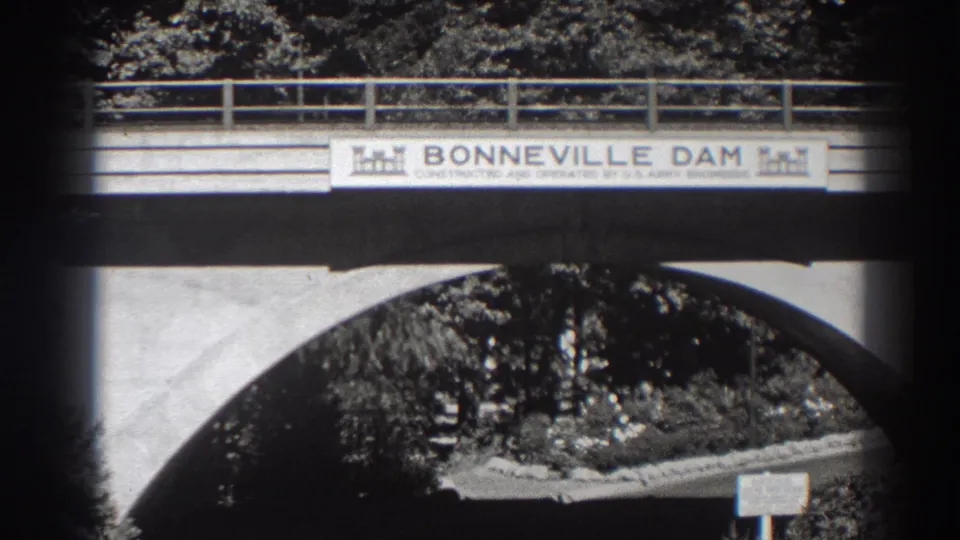Bonneville Dam sign remains centered on the bridge, with concrete supports, railings, and foliage visible in the 8mm frame.