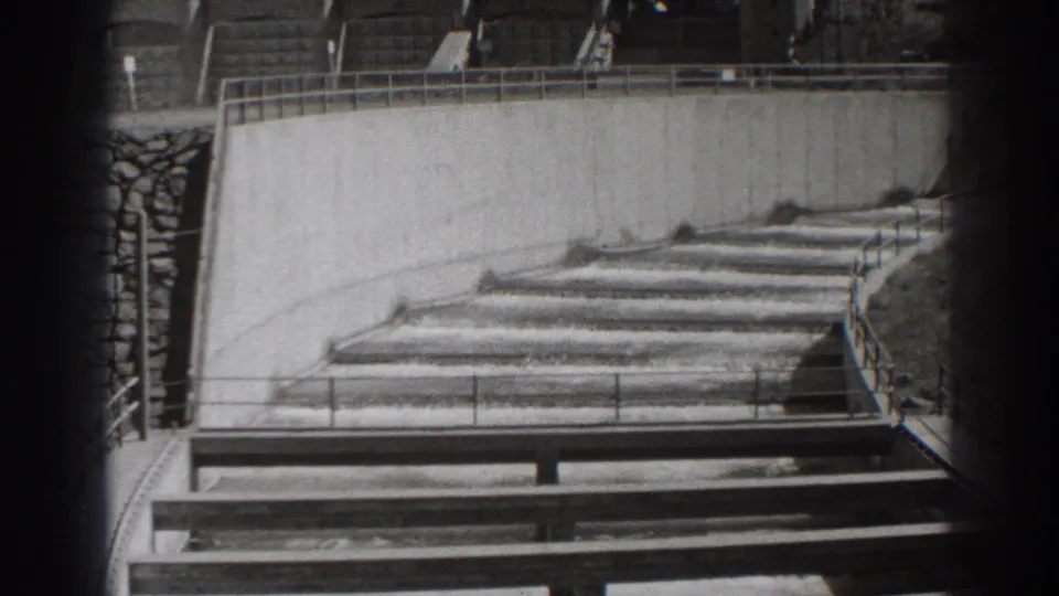 Bonneville Dam fish-ladder channels in Oregon, shown in black-and-white 8mm footage with railings and concrete walls.
