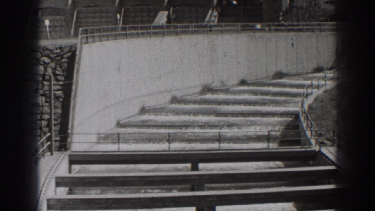 Concrete channel steps with water flow, railing, wall, and shadows.