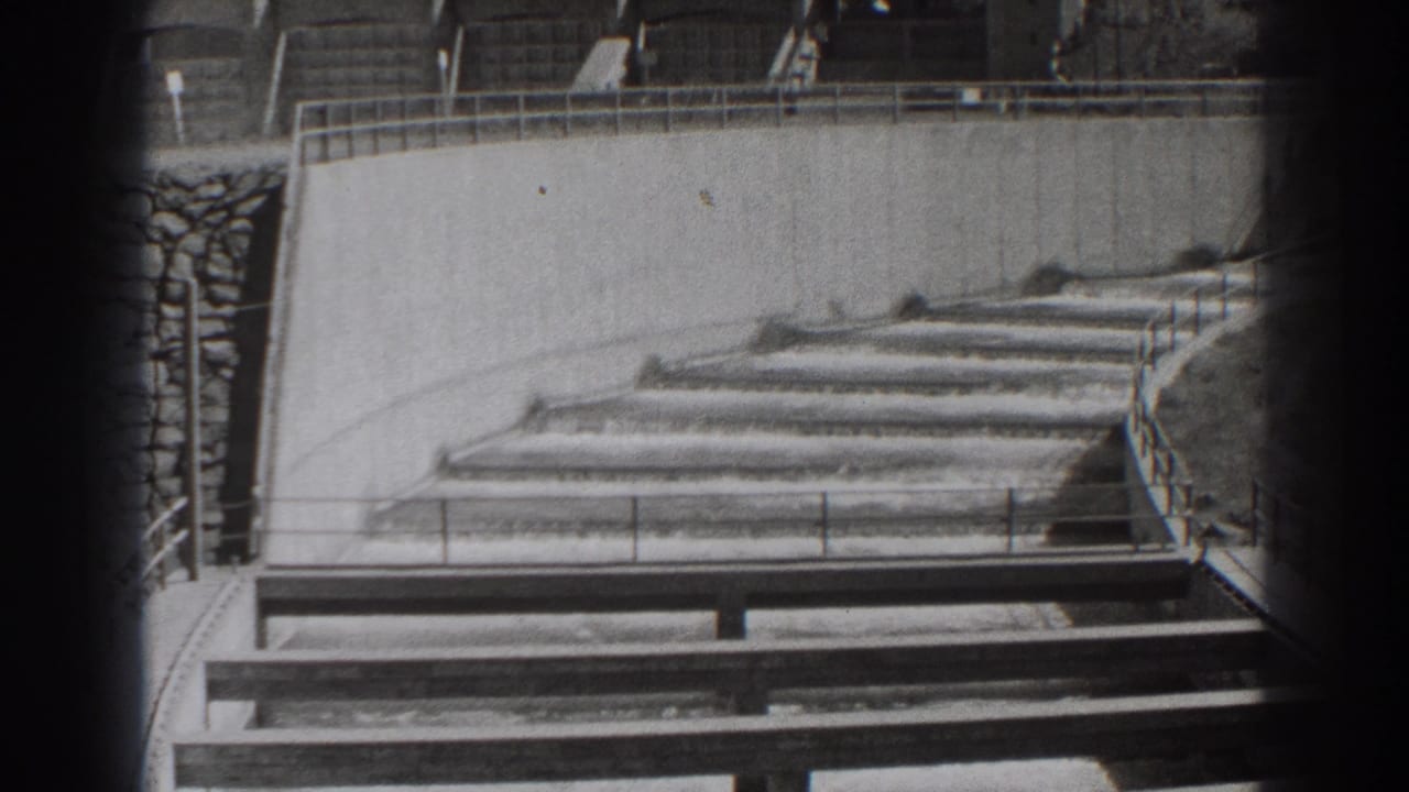 Stepped concrete spillway section with railings and dark film-frame edges.