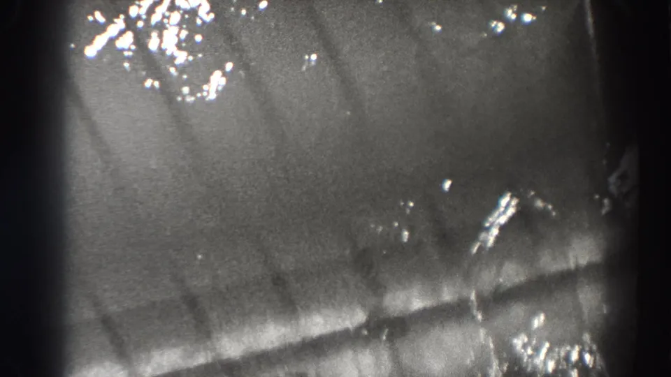 1938 Bonneville Dam 8mm frame showing rippling water, scattered highlights, and faint fish silhouettes beneath the surface.