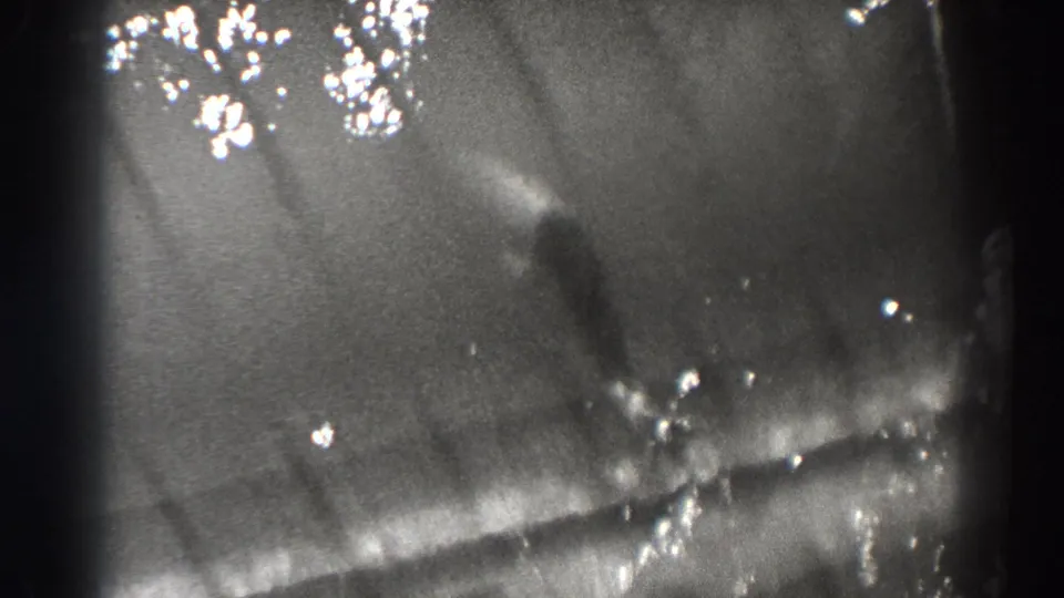 Bonneville Dam 1938 home-movie frame with a fish-like shape under dark rippling water and scattered white reflections.