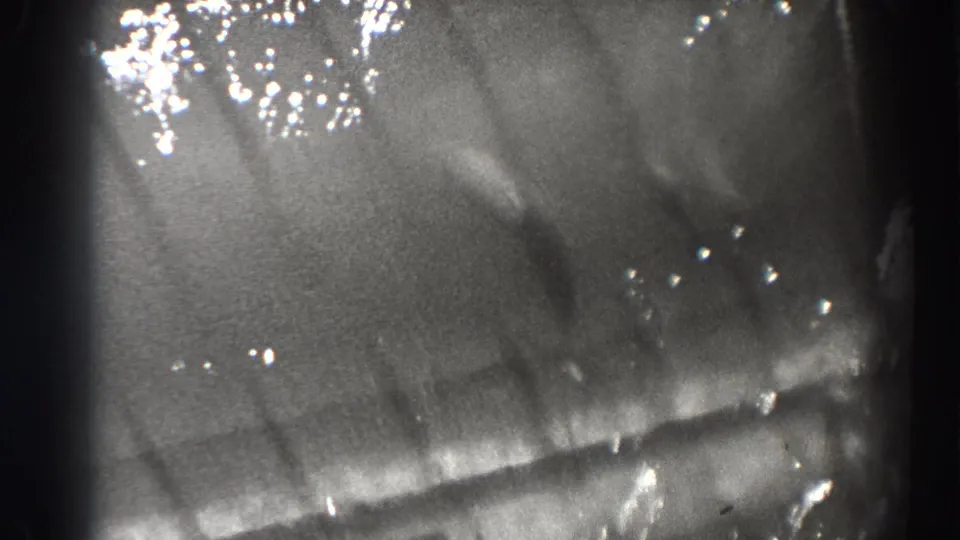 Grainy 1938 Oregon frame showing reflective current, small bubbles, and indistinct fish forms beneath the water surface.