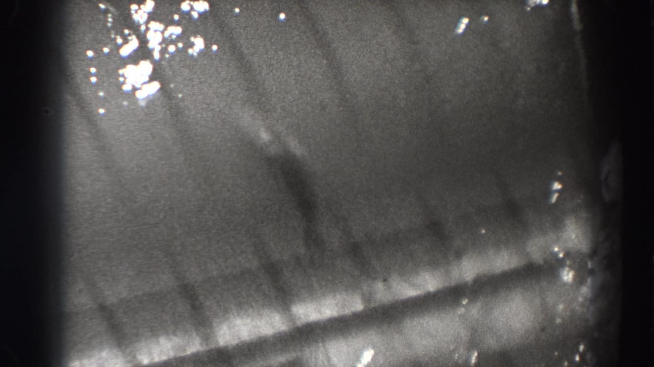 Fish-shaped shadow beneath rippled water with bright surface reflections and 8mm frame edges.