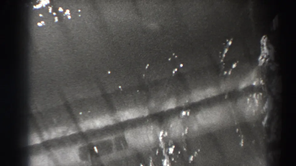 1938 Bonneville Dam home-movie frame showing a fish-like form near ribbed structure and reflective water in black-and-white 8mm.