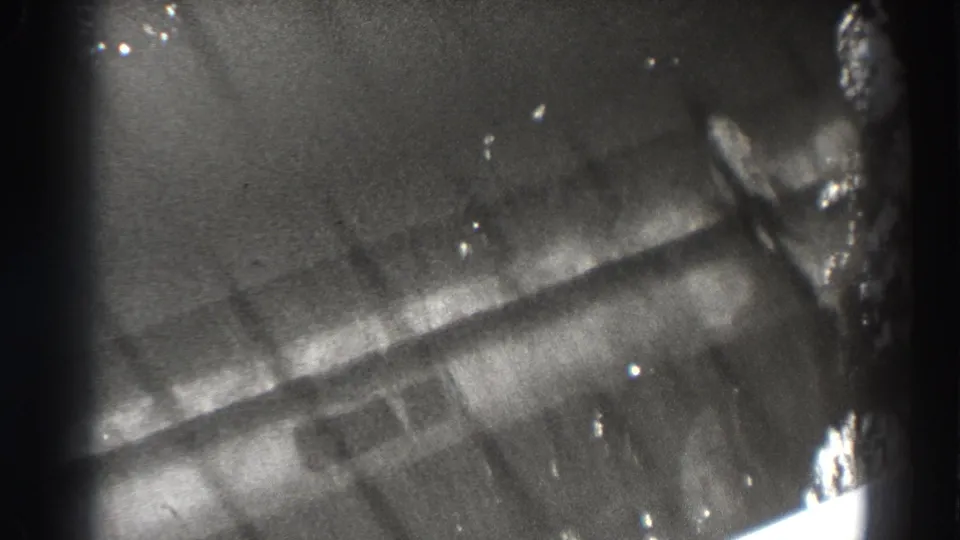 Black-and-white 8mm Bonneville Dam frame showing a fish-like form near ribbed structure, with heavy glare and dark film edges.