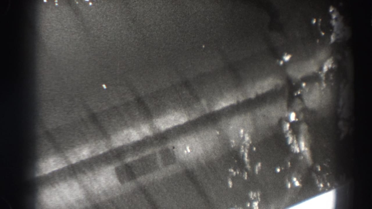 Soft black-and-white close view of water and dam structure seen through dark film-frame edges.