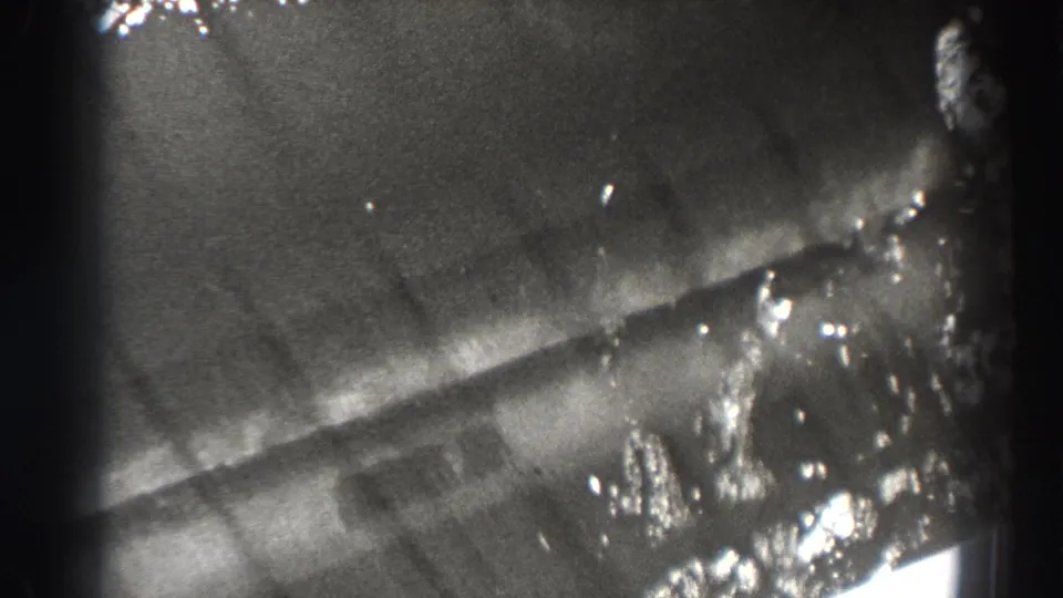 1938 Bonneville Dam home-movie frame with a partial close view of reflective water or dam surface and dark gate-edge shadow.