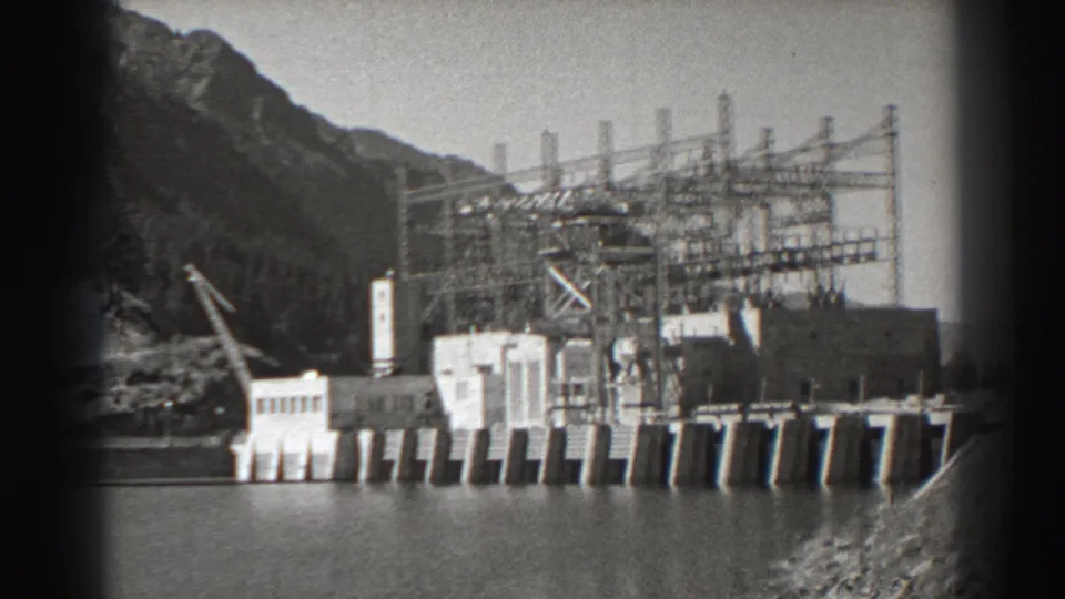1938 Bonneville Dam footage showing concrete riverfront structures, steel electrical framework, and mountain terrain in Oregon.