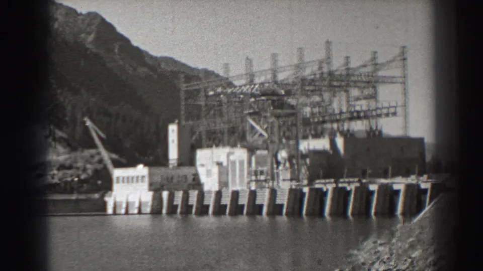 Bonneville Dam, Oregon, in black-and-white 8mm, with riverfront concrete works, lattice transmission towers, and wooded gorge slopes.