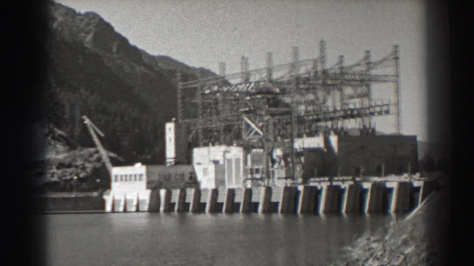 Black-and-white 8mm frame of Bonneville Dam in Oregon, showing the river, concrete spillway, transmission towers, and gorge landscape.