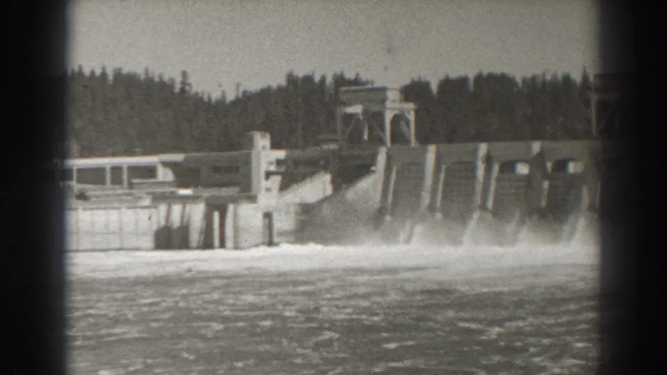 1938 Bonneville Dam view showing spillway water discharge, concrete control structures, and forested land beyond the dam.