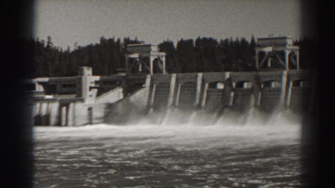 Concrete dam with several spillway sections releasing water into the river.