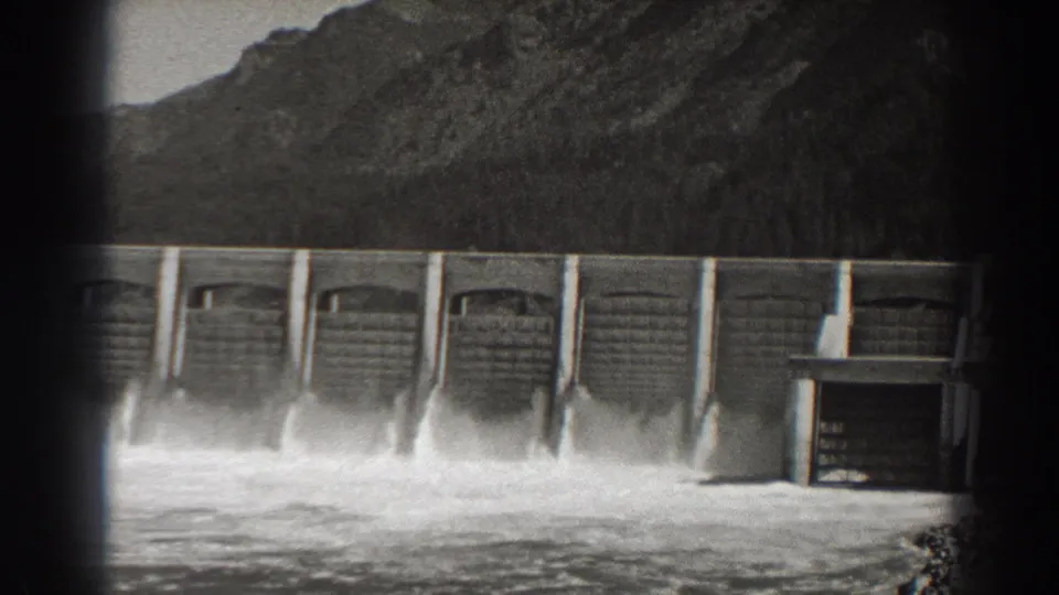 1938 8mm footage shows Bonneville Dam releasing water, with foaming flow below and a small structure near the right edge.