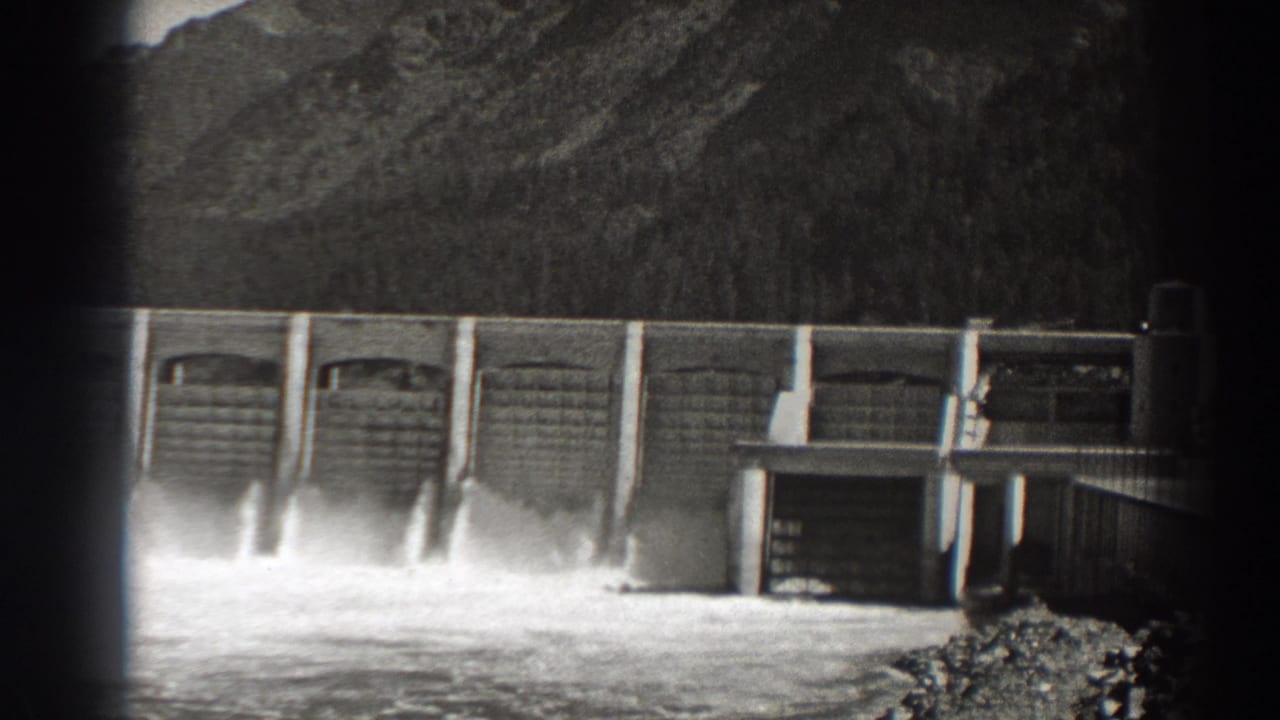 Dam spillways releasing water beside a small structure at right.