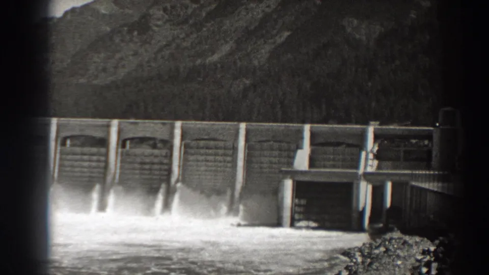 Bonneville Dam spillways release white water while a small service building appears near the right edge of the 8mm frame.