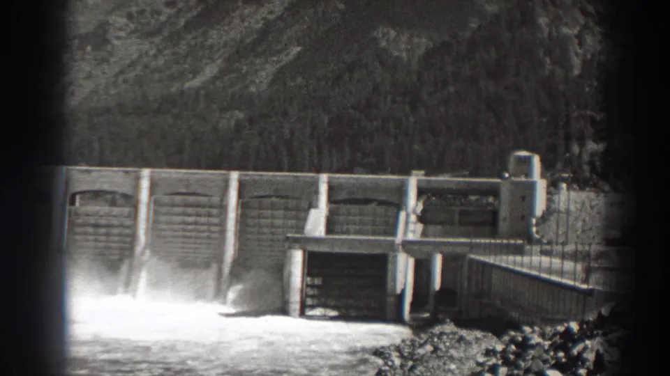 1938 Bonneville Dam view showing water pouring from a spillway below concrete gates, with forested slopes in the background.