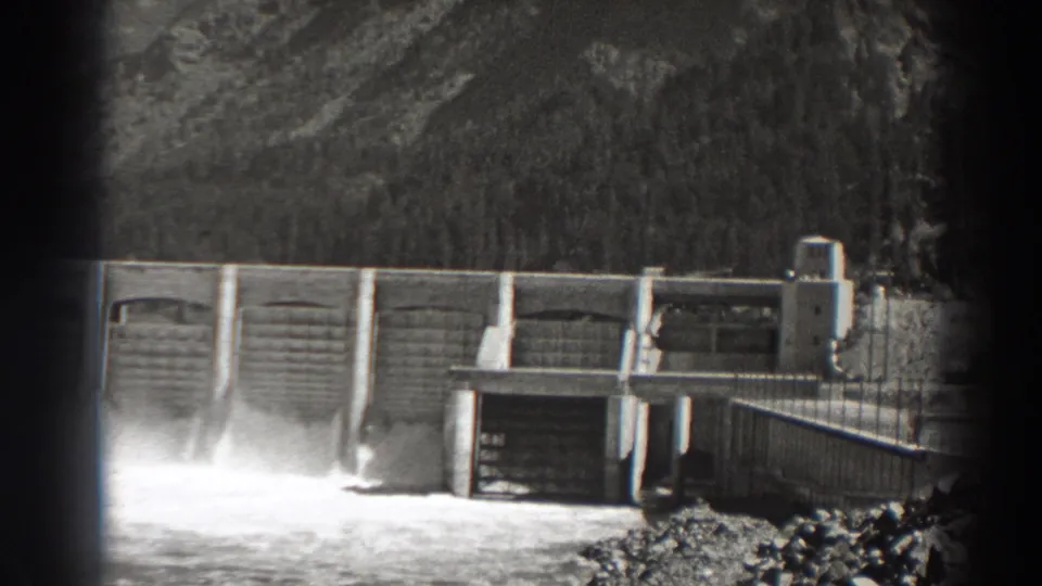 Bonneville Dam in Oregon, filmed in 1938, with water discharge visible beneath the concrete gate structure and trees beyond.