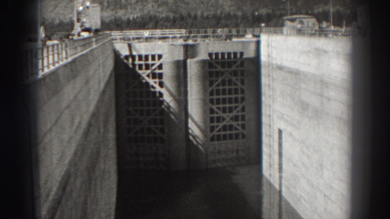 Gridded dam gates set between concrete walls with railings and dark foreground edges.