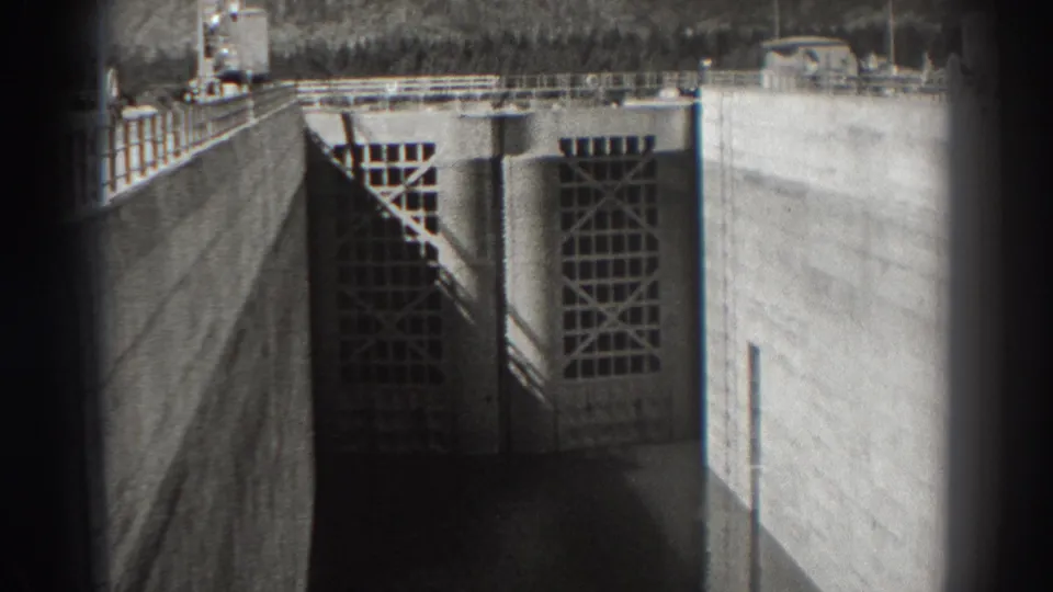 1938 Bonneville Dam view showing a large concrete floodgate with gridded panels, railings, and soft black-and-white 8mm framing.