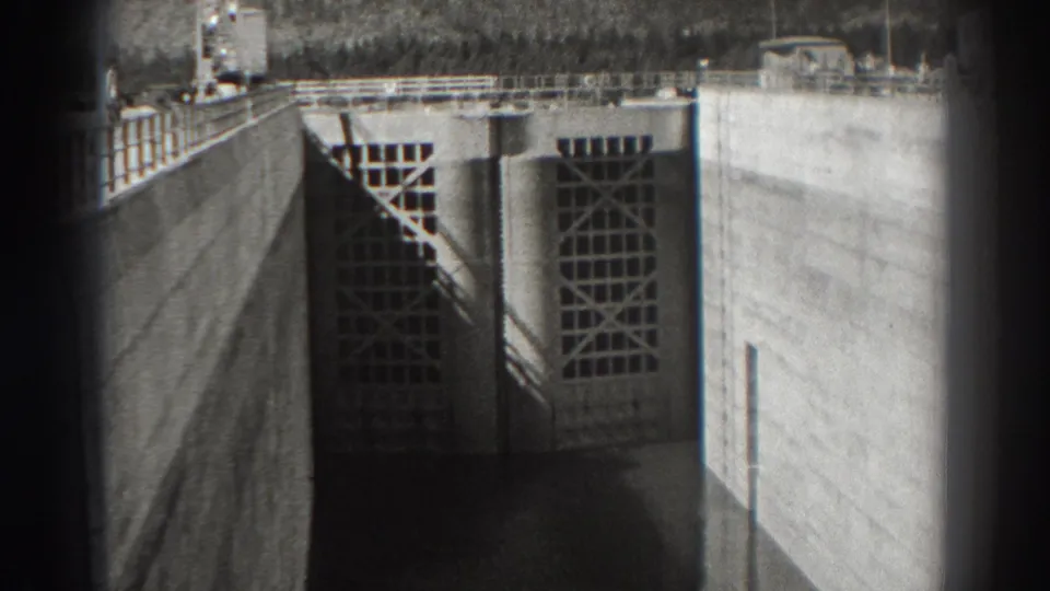 Bonneville Dam floodgate in 1938, with gridded gate panels, concrete walls, railings, and a dark rounded home-movie vignette.