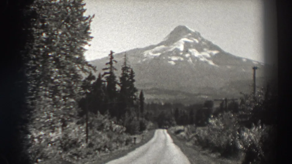 1938 Oregon home-movie frame showing the mountain larger in view above a winding rural road and forested foreground.