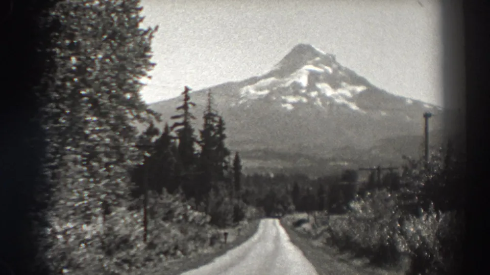1938 Oregon frame with a soft black-and-white view of a snow-capped mountain beyond evergreens and a rural road.