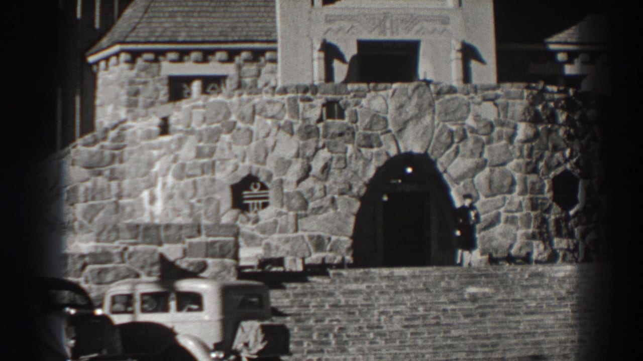 Stone castle-like building entrance with parked vintage cars in front.