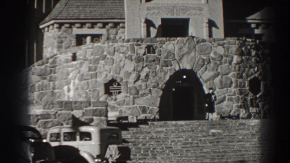 1938 Bonneville Dam area home-movie frame showing a stone building entrance, arched doorway, and parked period cars.