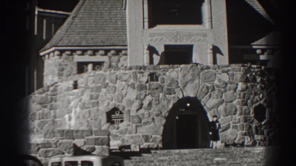1938 Bonneville Dam area frame with castle-like stonework, parked cars, and a person near the doorway.