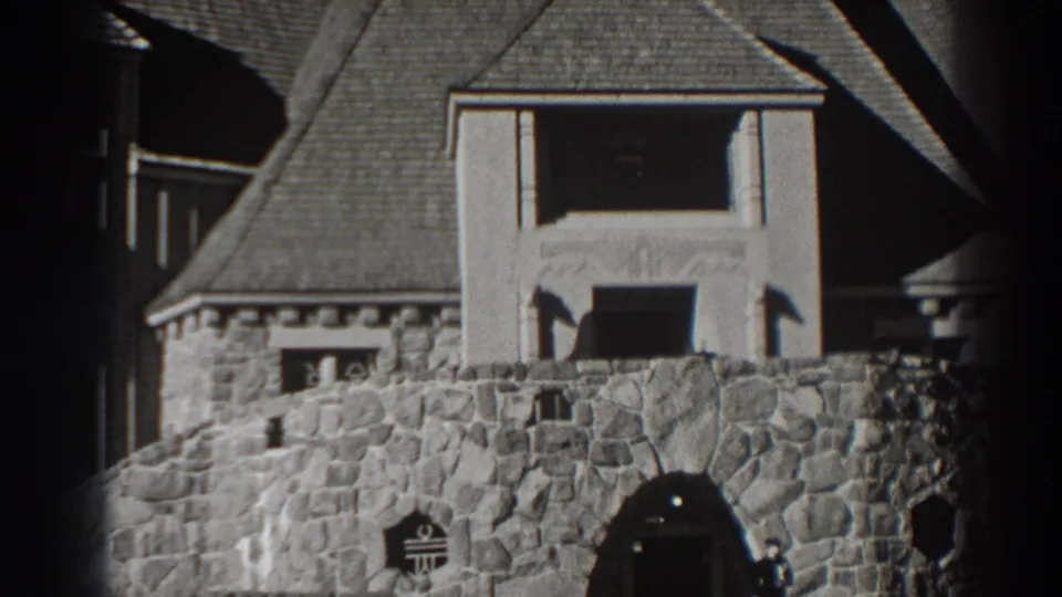 Home-movie frame from the Bonneville Dam area showing steep roofs, stonework, and part of the arched entrance.