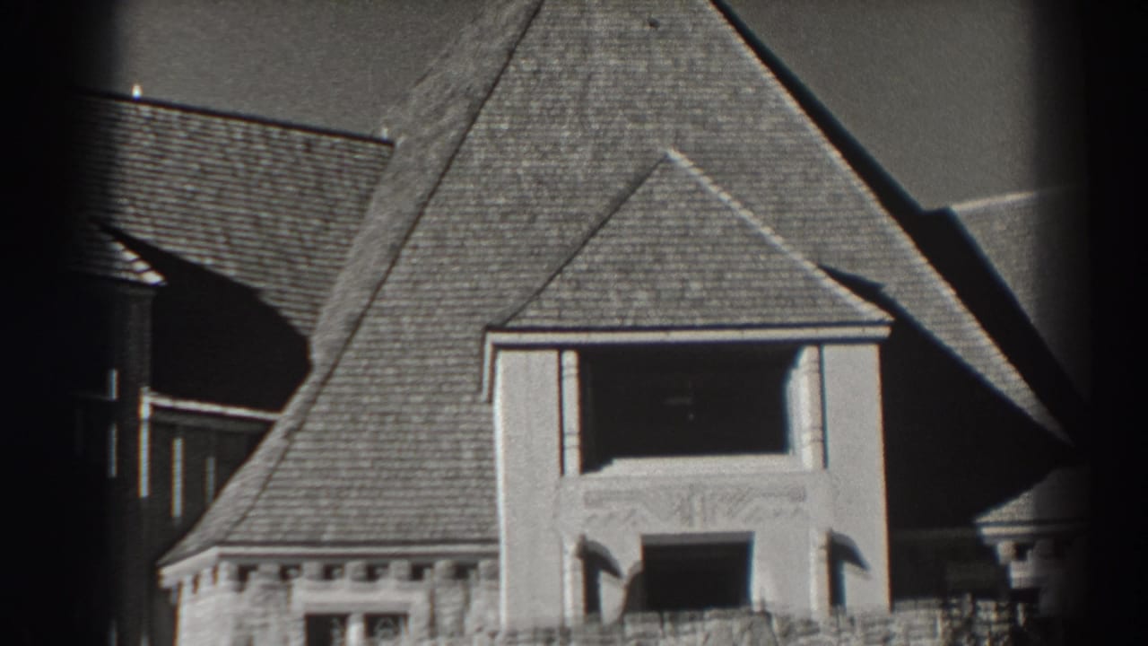 Close view of a steep shingled roof with masonry trim and a dark upper window.