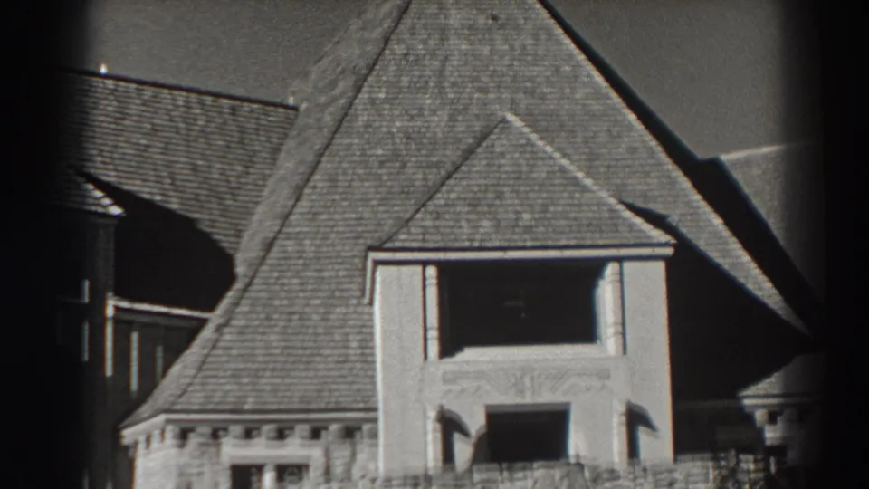 1938 Bonneville Dam building detail with steep roof shingles, pale masonry, and a shadowed upper window.