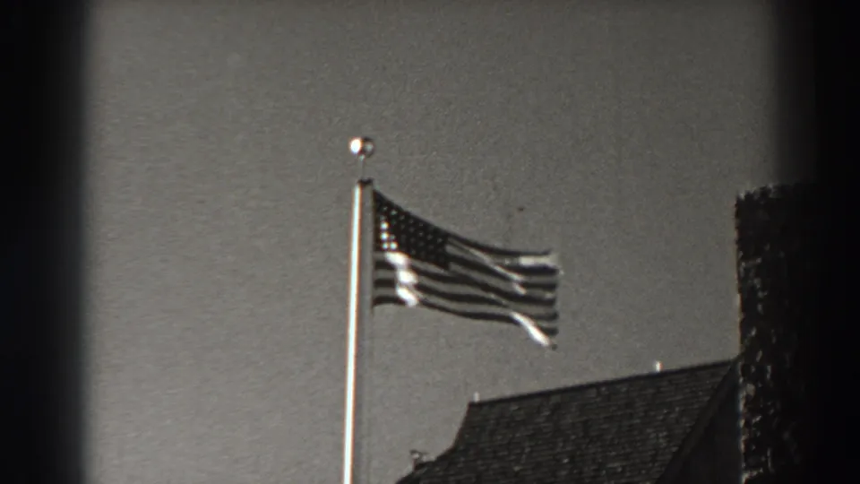 American flag flying from a tall pole above rooflines in the 1938 Bonneville Dam, Oregon home-movie footage.