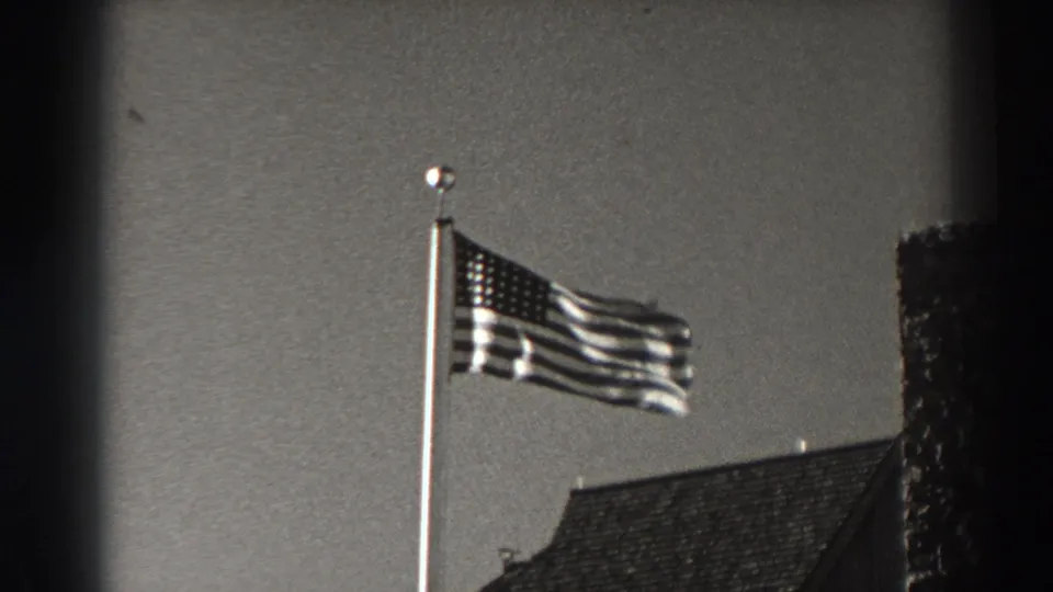 Bonneville Dam, Oregon home-movie frame showing the American flag on a pole, roofline below, and dark edge vignette at side.