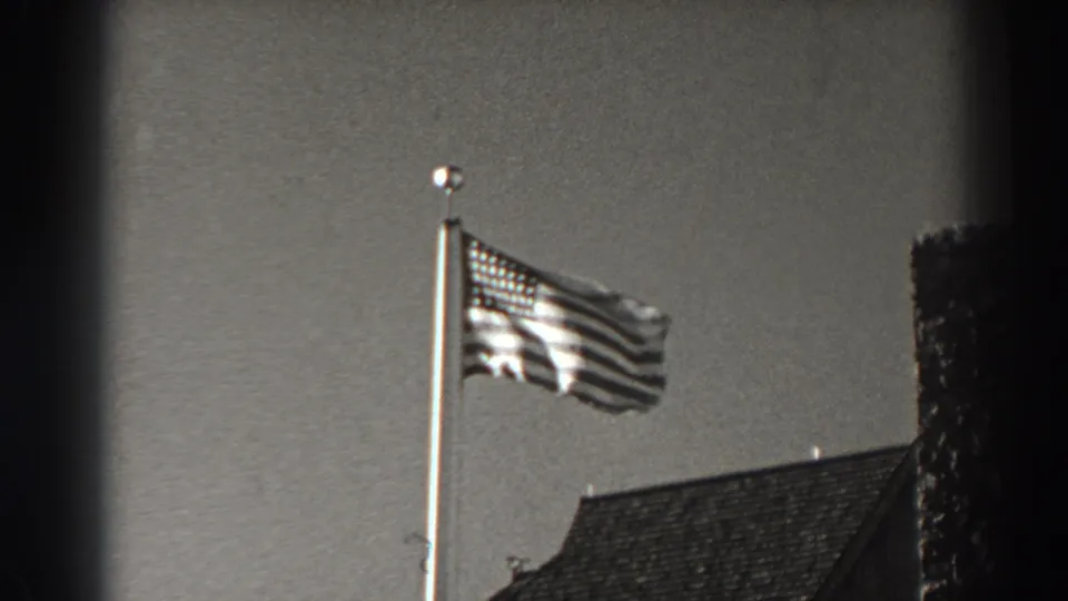 Late frame of the 1938 8mm Bonneville Dam view, with the American flag waving above a roof and dark frame borders visible.