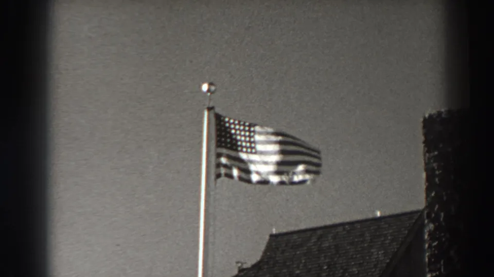 A U.S. flag flies at full staff above a roofline in 1938 Bonneville Dam-area 8mm footage.