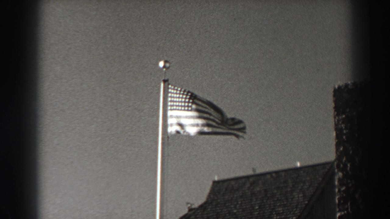 U.S. flag extended in the wind beside a roof and dark vertical edge.