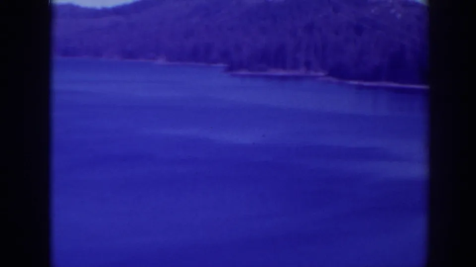 Blue-cast 1938 Bucks Lake frame with lake water in front of a dark forested mountain slope.