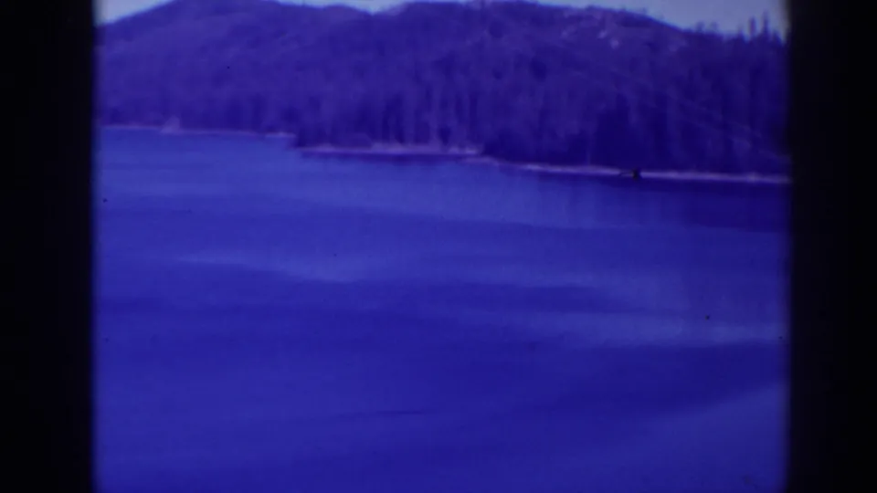 Late frame from the 1938 Bucks Lake pan showing blue water, tree-lined shore, and a dark mountain ridge.