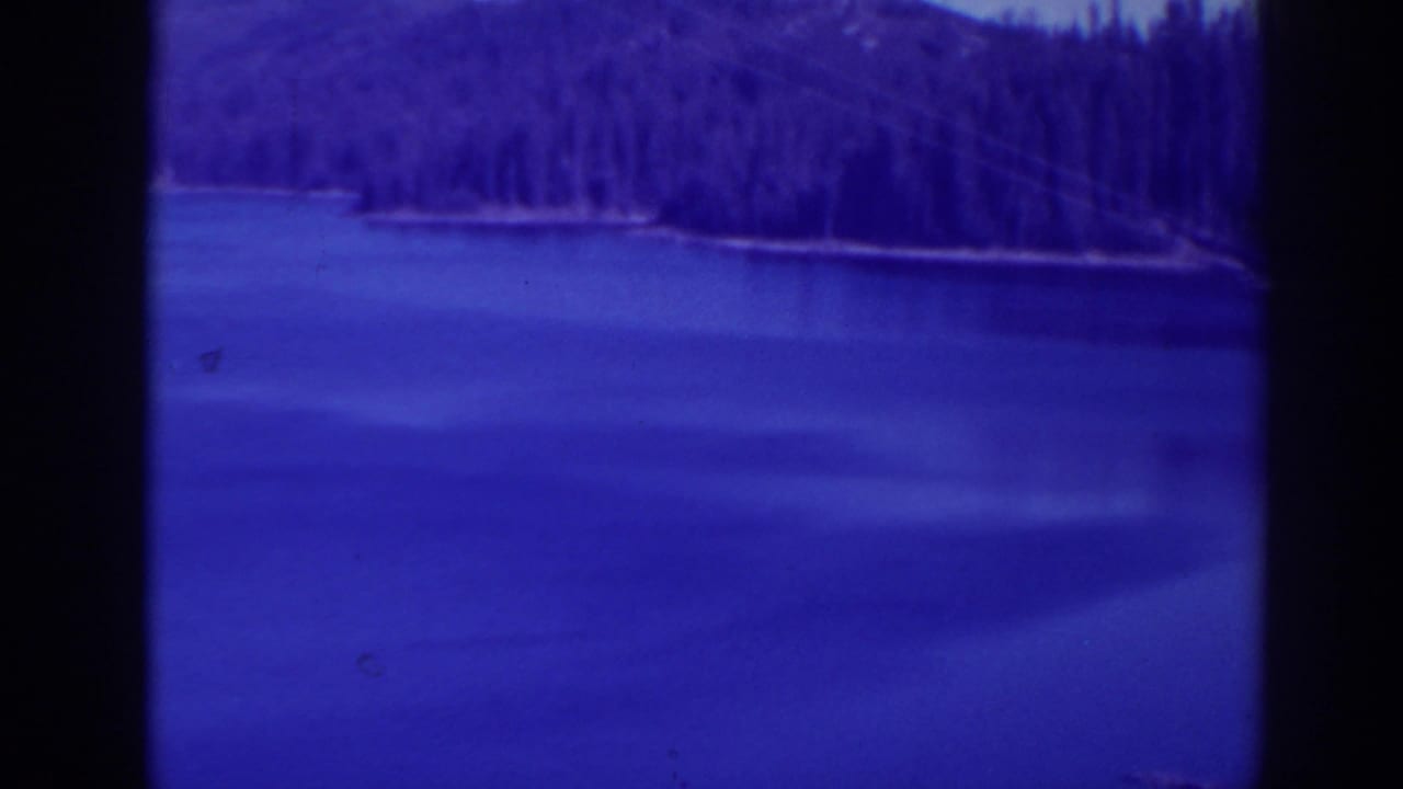 1938 Bucks Lake, California home-movie frame showing calm lake water, distant evergreens, and pronounced blue-purple film tint.
