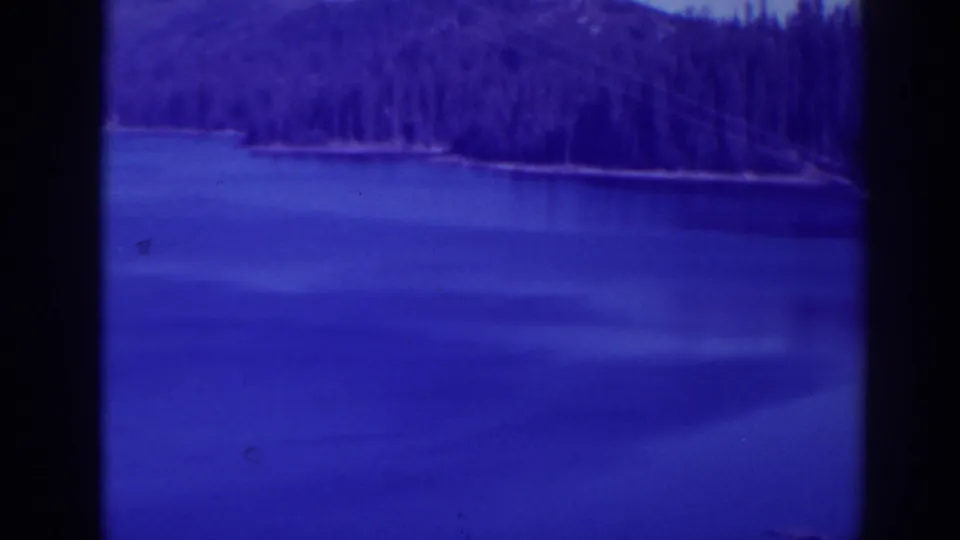 1938 Bucks Lake, California home-movie frame showing calm lake water, distant evergreens, and pronounced blue-purple film tint.