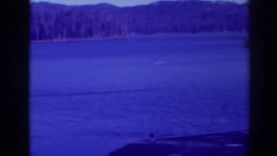 1938 Bucks Lake home-movie frame showing a small boat on calm blue water below a distant evergreen shoreline.