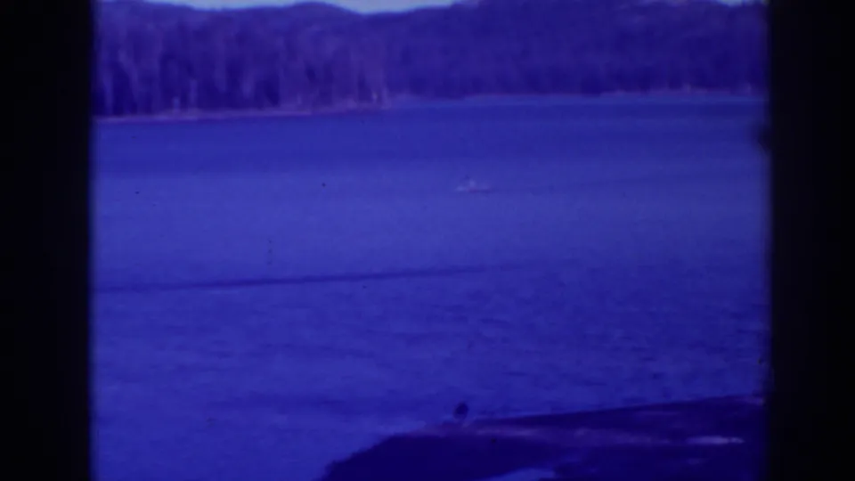 Bucks Lake, California, in 1938, with a tiny boat on blue water and evergreen shoreline beyond.