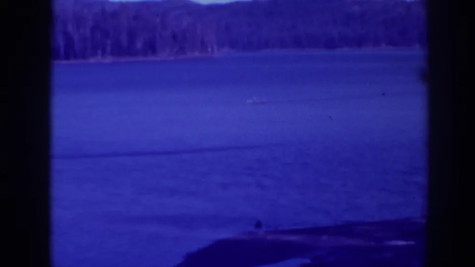 Vintage 8mm view of a small boat on Bucks Lake, framed by dark foreground edges and a wooded shoreline.
