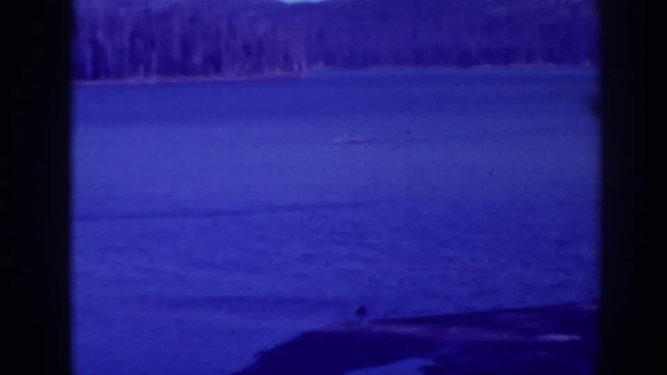 Late-1930s Bucks Lake frame with a small boat crossing calm water under a hazy forested horizon.