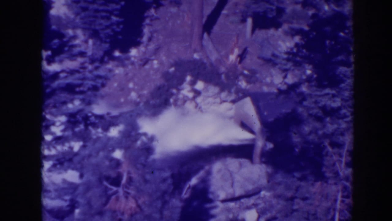 Water jet rushing from a rocky forested area with dark film borders.